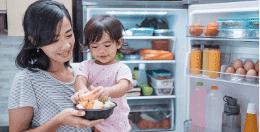 Mother and daughter holding a bowl of fruit in front of a fridge with the door open | The Good Guys