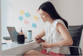 Lady sitting at her desk looking at her phone with a speaker.|The Good Guys