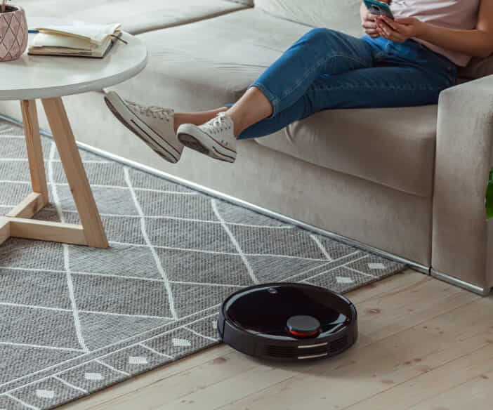 Robot vacuum transitioning from cleaning a rug to cleaning wooden floorboards.