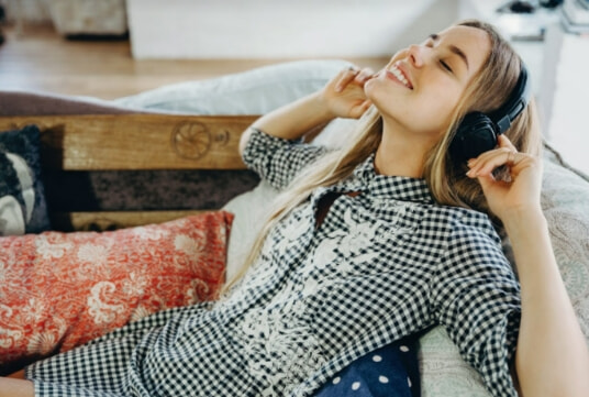 Female relaxing on a couch with over ear headphones on.