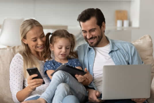 Family sitting on a couch with a laptop, tablet and mobile phone. 