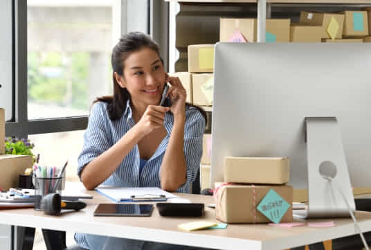 Lady on her phone whilst looking at her desktop computer screen.