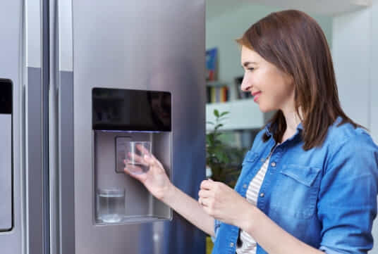 Women filling a cup up with water from the water dispenser on her fridge. 