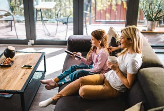 Mother and daughter sit down on couch to watch some TV
