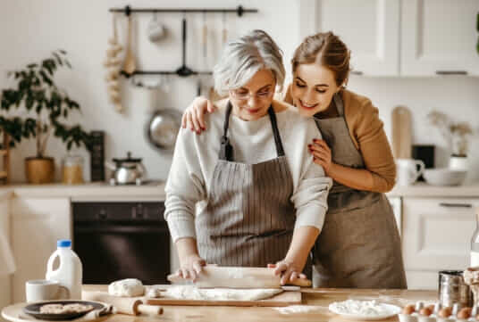 Older Mother and adult daughter bake in kitchen together