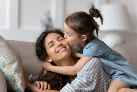 Girl giving her Mum a kiss on the cheek to wish her a Happy Mothers Day