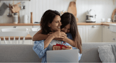 Daughter giving her mum a hug and a wrapped gift this Mother’s Day at home. 