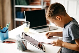 Child writing on a notepad whilst also having his iPad in front of him. 