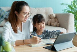Mother and daughter writing in a notebook whilst also looking at a tablet screen.