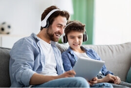 Two males with headphones on watching something on their device. 