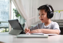 Young boy writing whilst also looking at his tablet.  