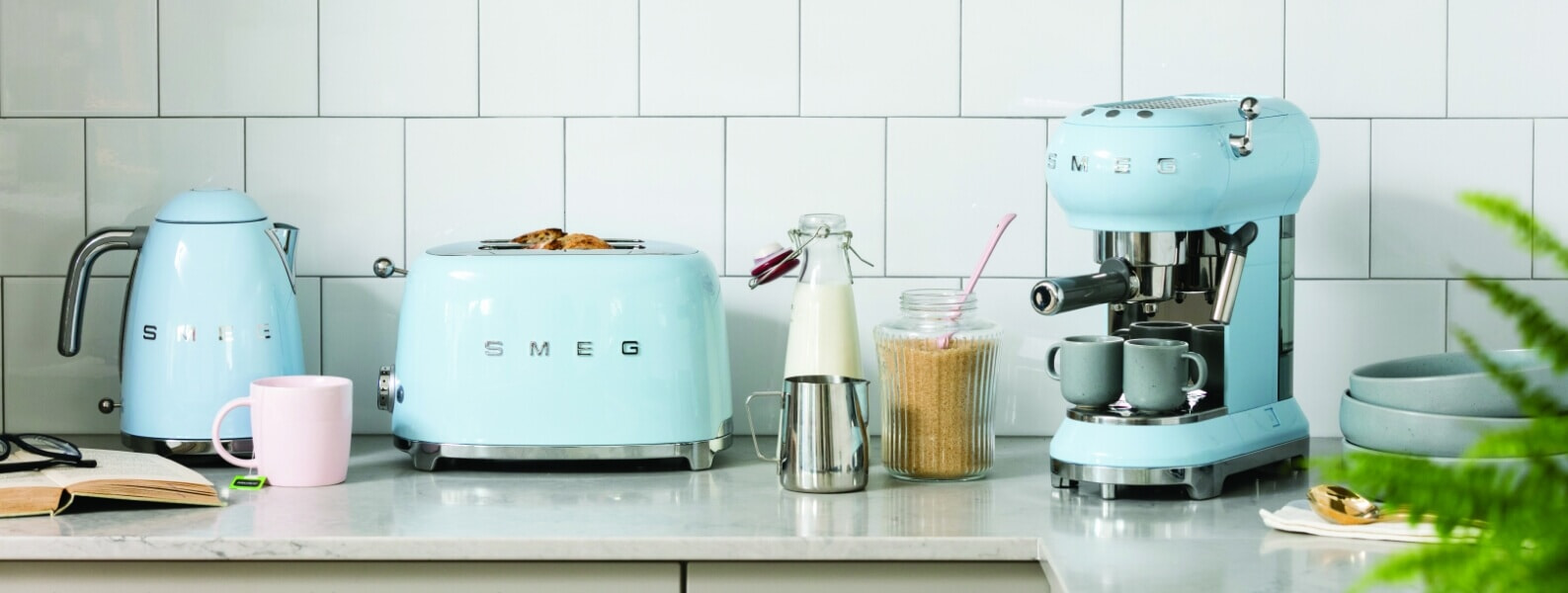 Matching pale blue retro Smeg small kitchen appliances, including a kettle, toaster, and a coffee machine on a grey kitchen bench