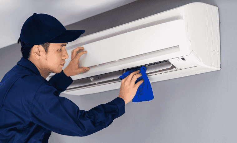 Man in navy shirt servicing an air conditioner.