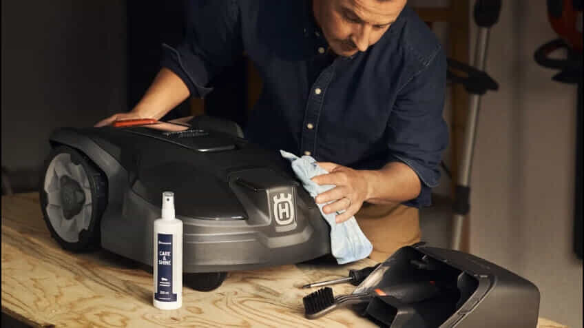 A man cleans his Husqvarna robot lawn mower with a cleaning kit.