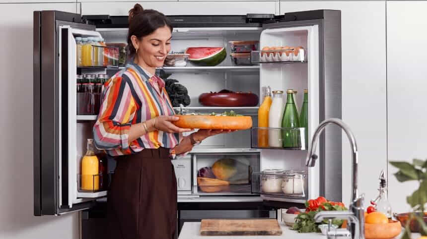 A woman stands in front of her open Samsung French door fridge, holding a platter.