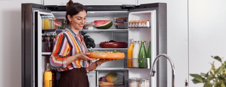 A woman holds a bowl in front of her Samsung 7000 series French door fridge.