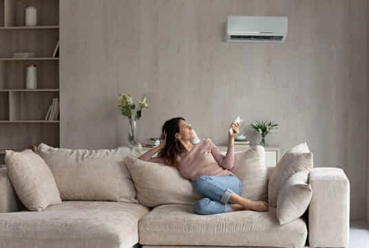 A woman adjusts the temperature of her split system air conditioner in her living room.