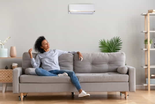 A woman relaxes in her living room as a split system air conditioner cools the room.