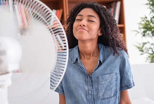 A woman cools herself in front of a fan