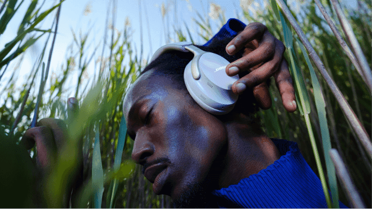A man using his Bose Quietcomfort Headphones in a field of long grass.