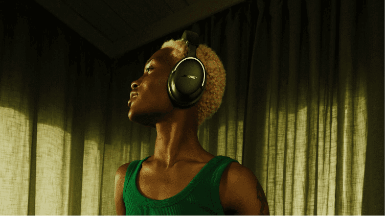 A woman standing on the side listening to her bose quiet comfort Ultra headphones