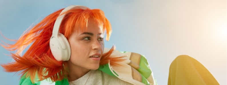 A woman with bright orange hair wears the Bose QuietComfort Headphones in white.
