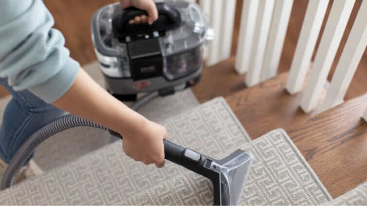 A person uses the Hoover ONEPWR CleanSlate Pet Cordless Spot Cleaner to clean the carpet on their stairs.