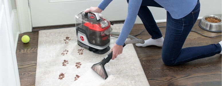 A woman spot cleans muddy pawprints off a rug with the Hoover CleanSlate SpotWasher.