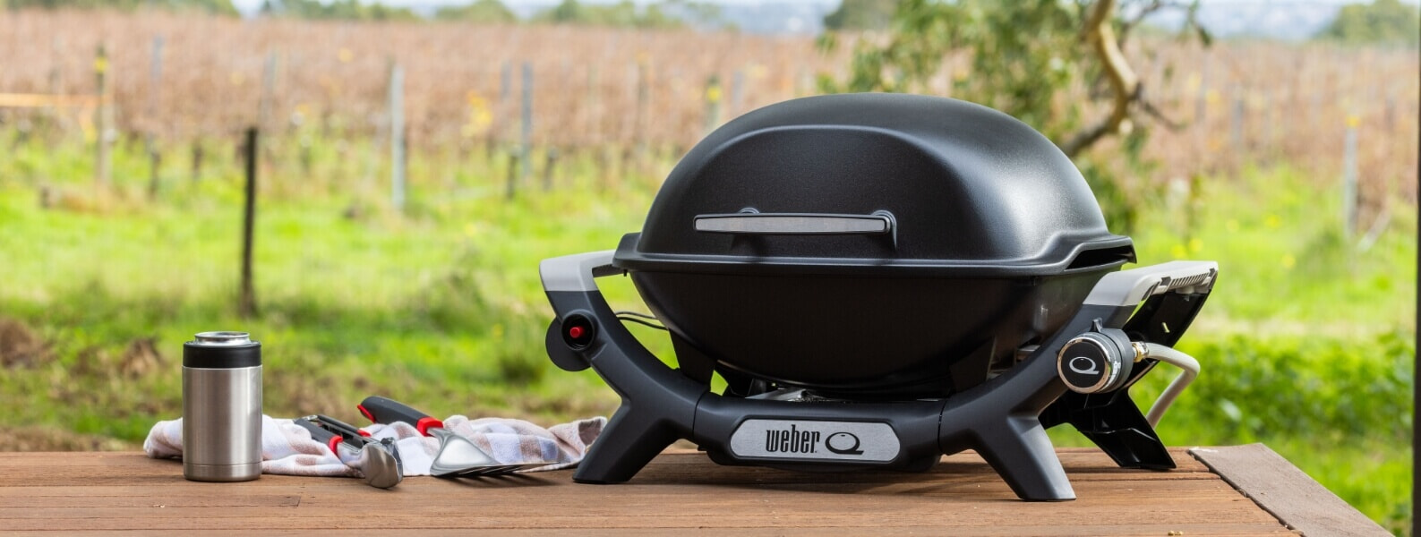 A black Weber Baby Q BBQ sits on a picnic table at a vineyard | The Good Guys