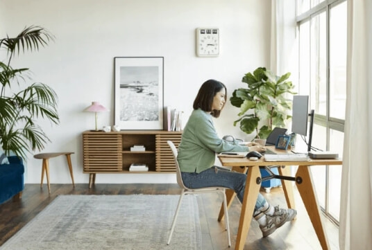 a woman uses her laptop attached to a second monitor in her home office.