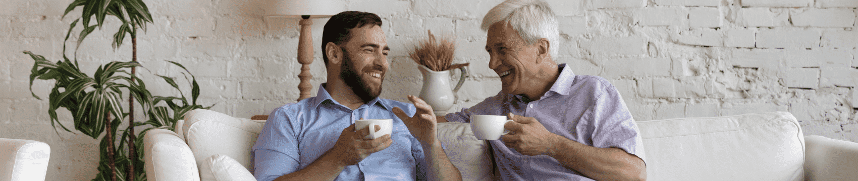 A father and a son sitting on the couch together enjoying a cup of coffee they made from home
