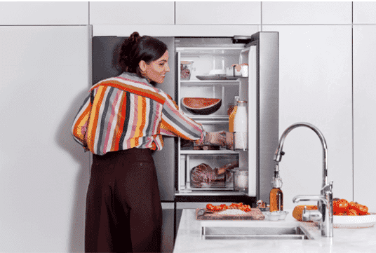 A woman reaches into the top right side of her Samsung French door fridge