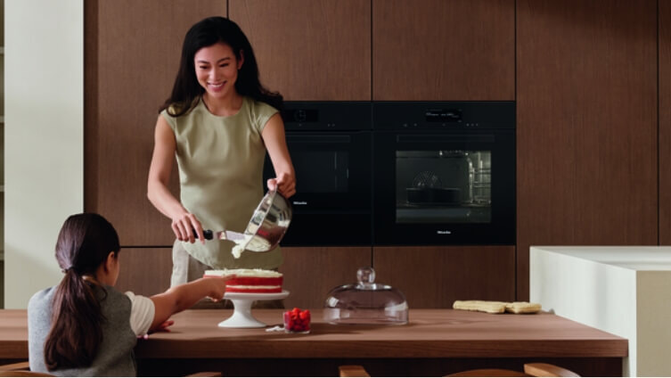 Woman cutting cake in front of Miele Ovens.