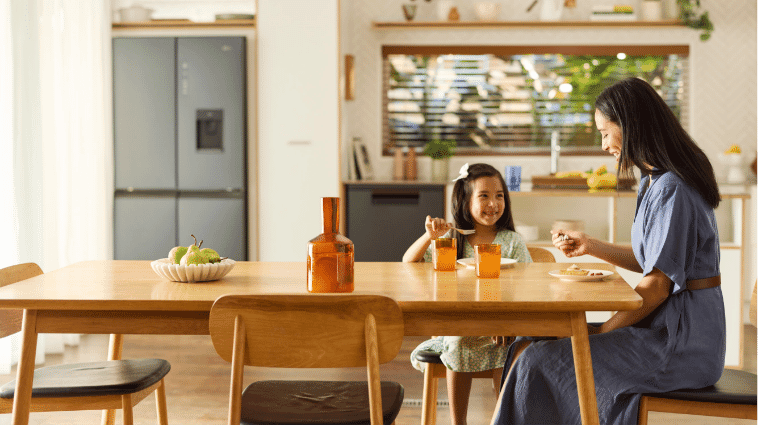 Mother and daughter eat at table whilst Haier Dishwasher quietly cleans.