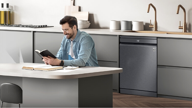 Man reads book in kitchen next to LG's QuadWash Dishwasher