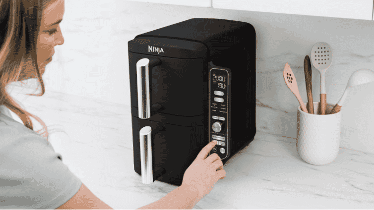 Image of a woman using the Ninja® DoubleStack™ XXXL 2 Drawer Air Fryer on a kitchen bench.