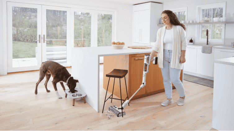 Image of a woman using a Shark stick vacuum to clean her kitchen floor.