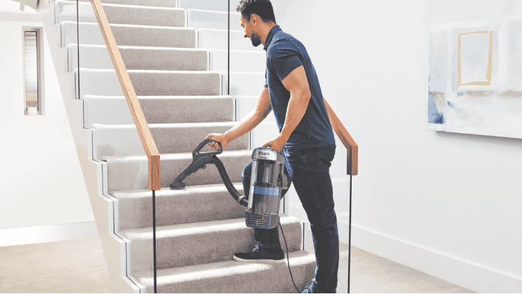 Image of a man using a Shark upright vacuum to clean carpeted stairs.