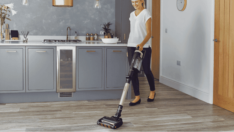 Image of a woman using a Shark pet vacuum to clean kitchen floor.