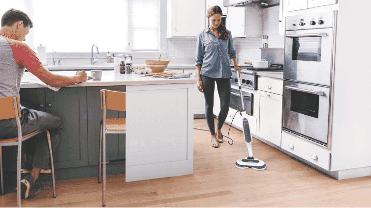 Image of woman using a Shark steam mop to clean kitchen floor.