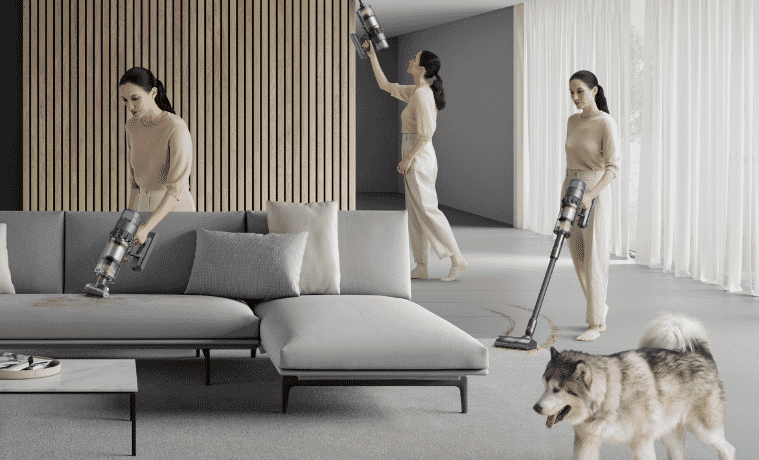 3 versions of the same woman walk around a living room, using the different modes of a Dyson stick vacuum.