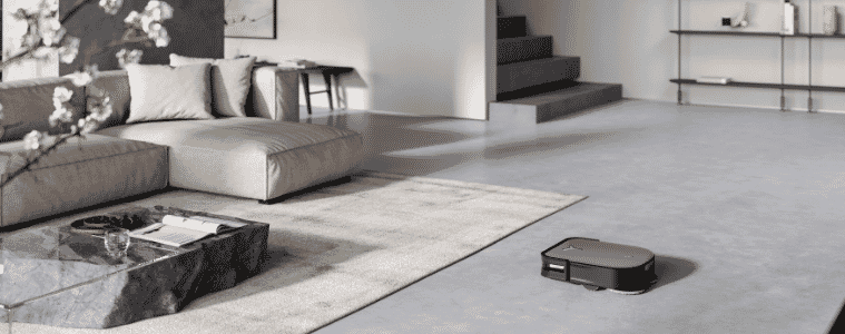 Square robot vaccuum in action on concrete floor. 
