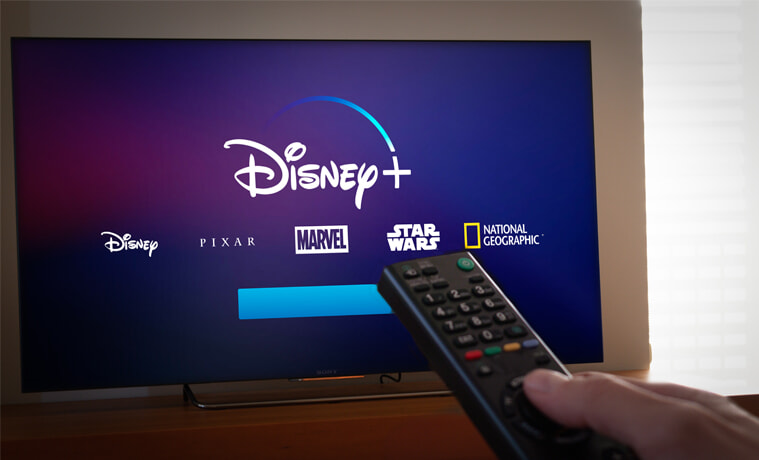 A person uses a remote to navigate to Disney Plus on their TV.