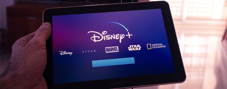 A man holds a tablet displaying Disney Plus
