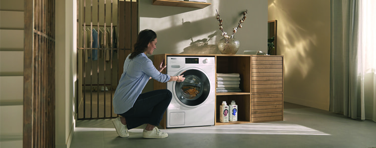 A woman uses her Miele washing machine in a light and airy laundry.