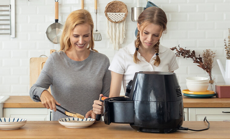 A father, mother, daughter and son cook together in their family kitchen, using an air fryer. 