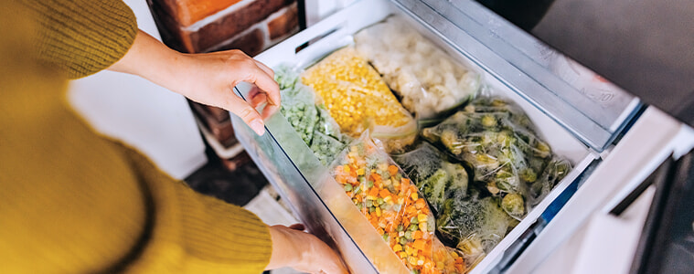 Woman putting a container with frozen mixed vegetables into the drawer of her fridge-freezer. 