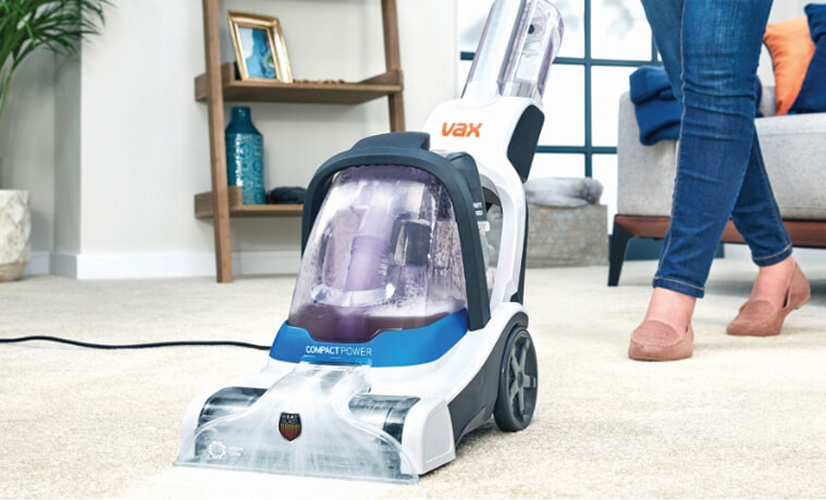 A woman cleans her living room carpet with the Vax Compact Power Carpet Cleaner.
