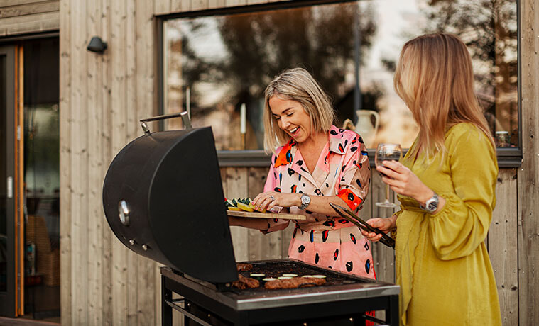 Smiling female friends prepare food on a barbecue.
