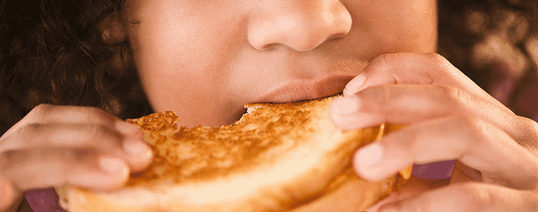 Close-up of a young girl eating a toasted sandwich.